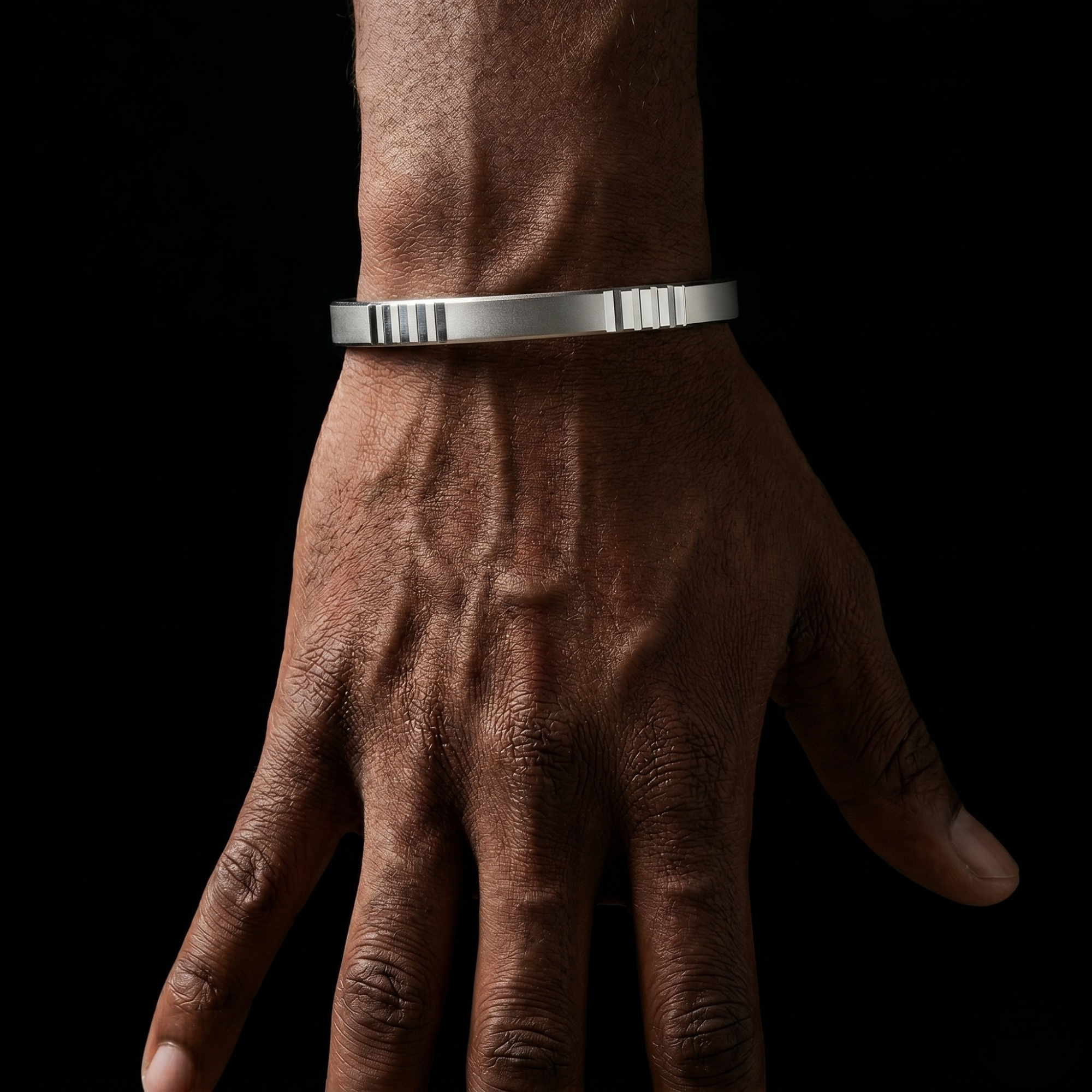 Hand wearing a silver bracelet against a black background