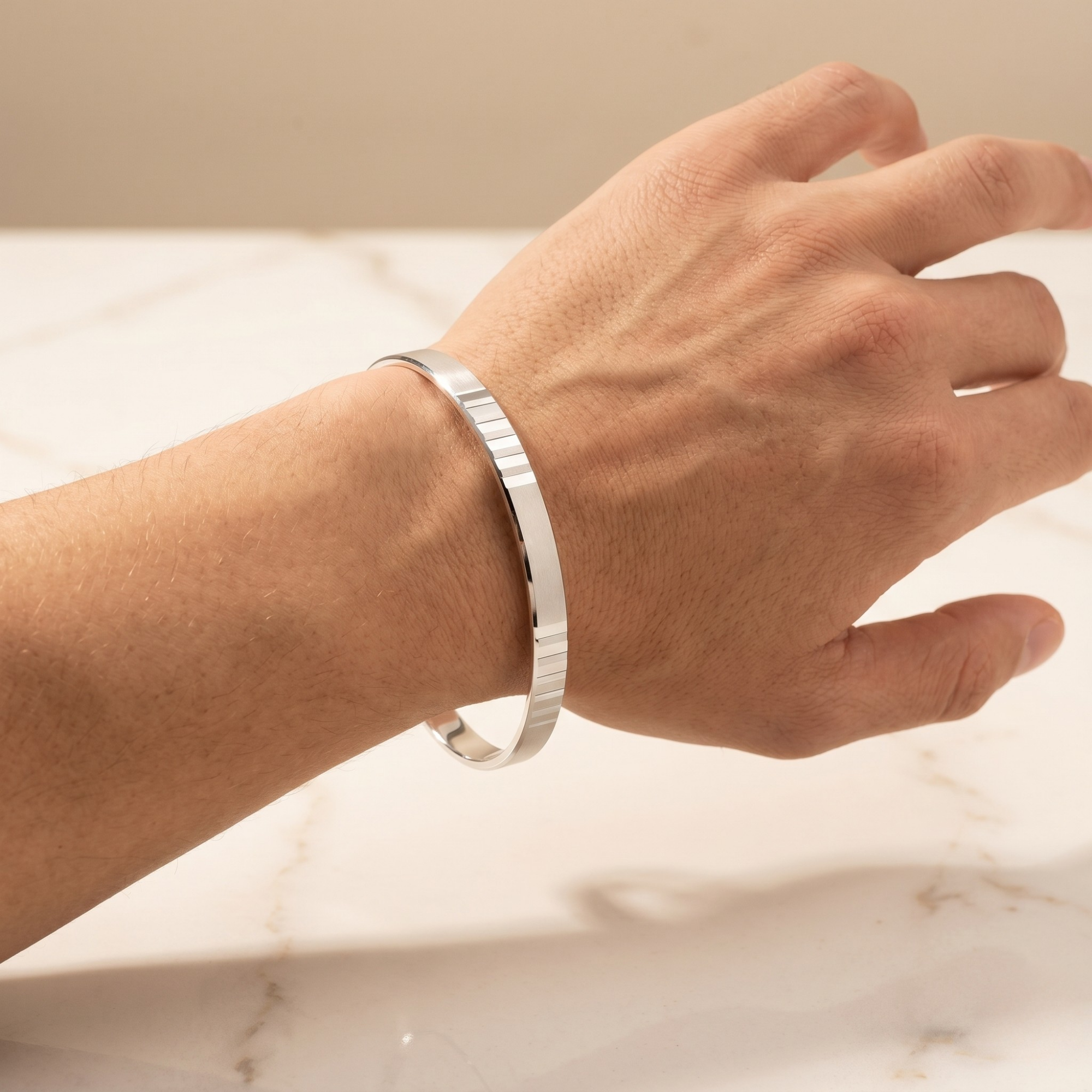 Silver bracelet on a wrist against a neutral background