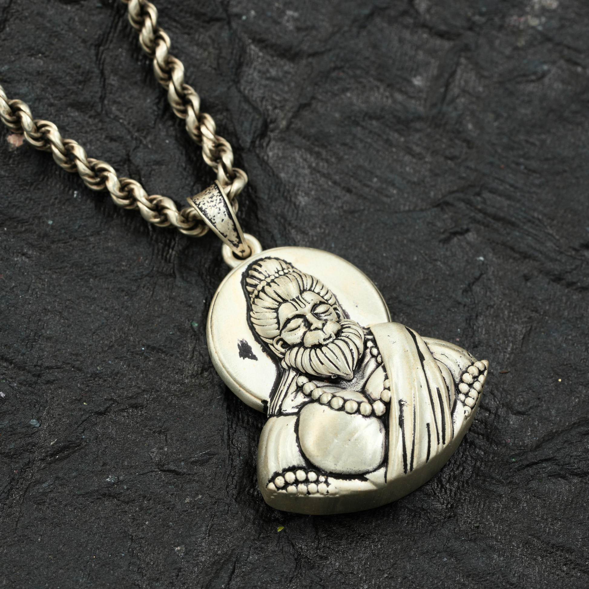 Silver pendant of a hanuman on a black stone surface